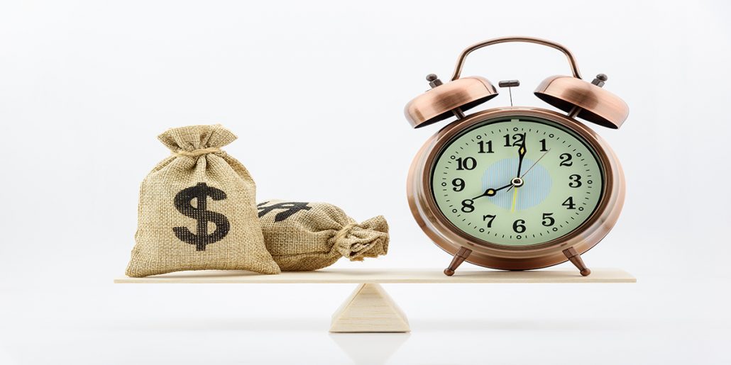 Two burlap bags with dollar signs on a balancing apparatus with an alarm clock on one end.